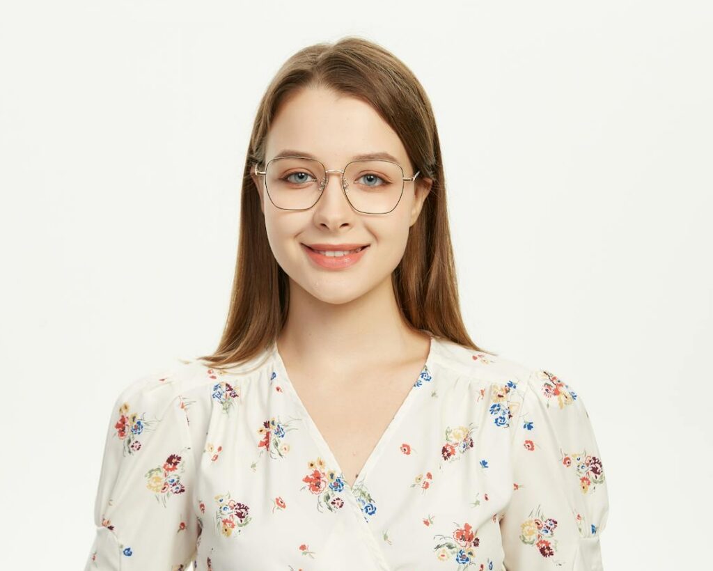 Young woman wearing glasses smiling in a floral outfit against a plain background.